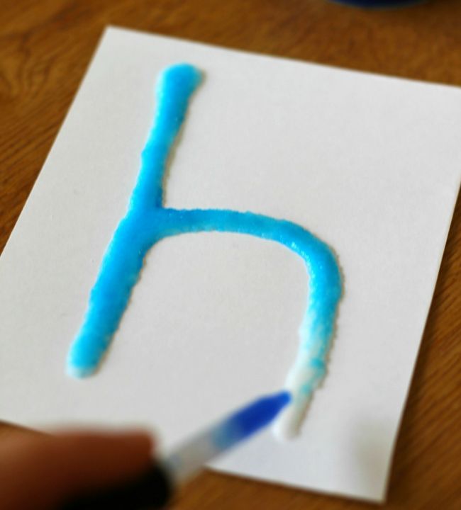 Kindergarten science student using a dropper to add blue water to a lowercase H made from salt and glue