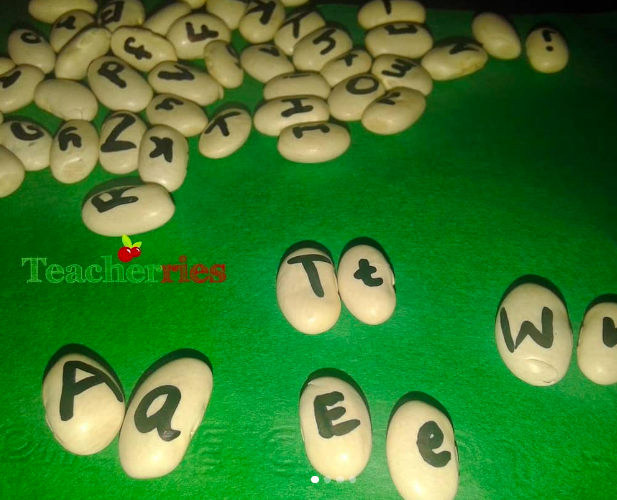 Dried beans, each with a letter of the alphabet written on it, spread out on a green background