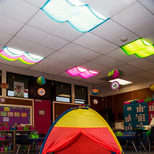 A tent is setup in a classroom. Overhead flourescent lights are covered with brightly colored fabric covers.