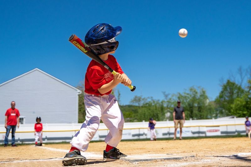 Small child waiting at home base for a baseball pitch that's about to arrive