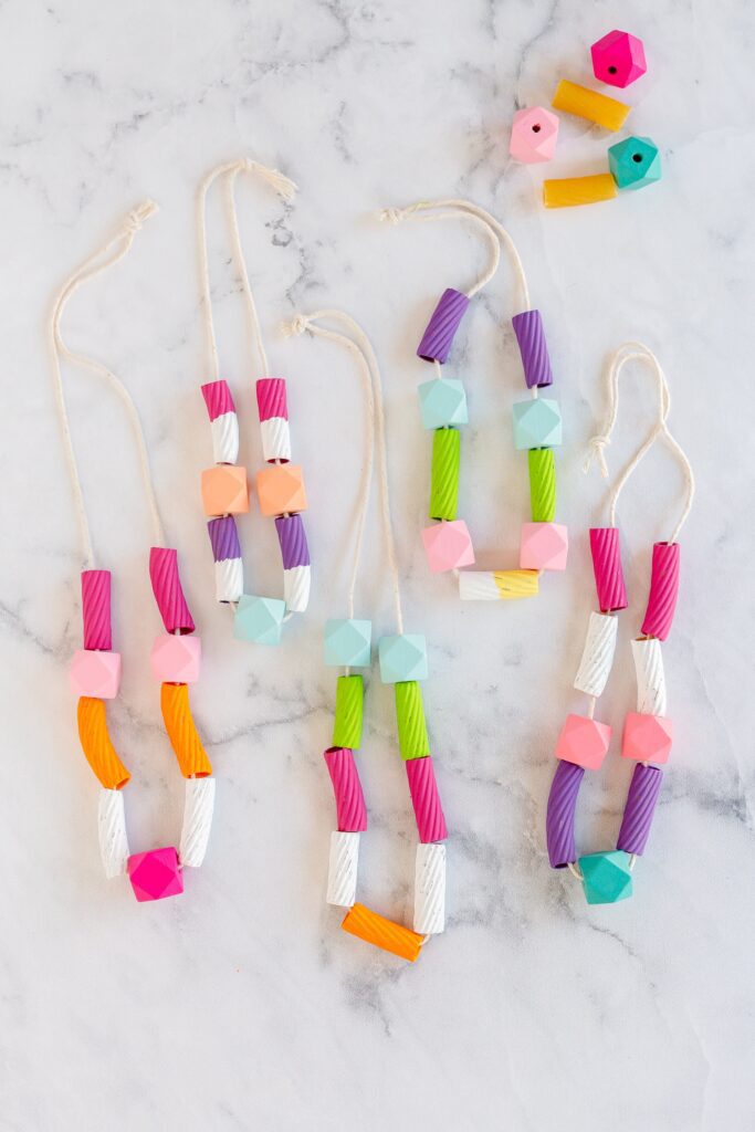 This easy art project for kids shows 5 multi-colored macaroni necklaces made from painted macaroni, string, and some beads.