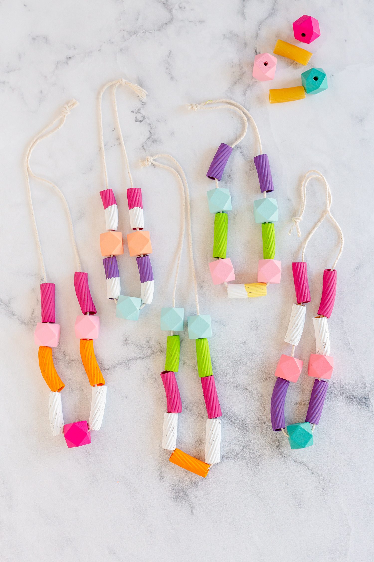 This image of an easy art project for kids shows 5 multi-colored macaroni necklaces made from painted macaroni, string, and some beads.