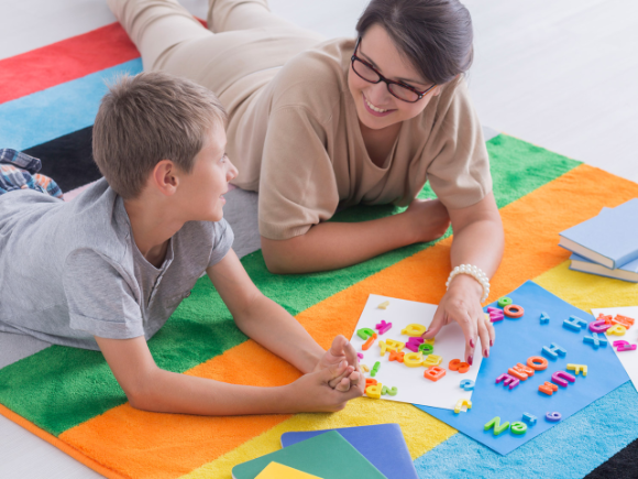 A teacher and student lay side by side on a mat as they make words with plastic letters