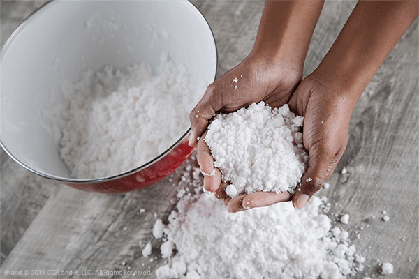 A hand is shown holding fake snow from a pile.