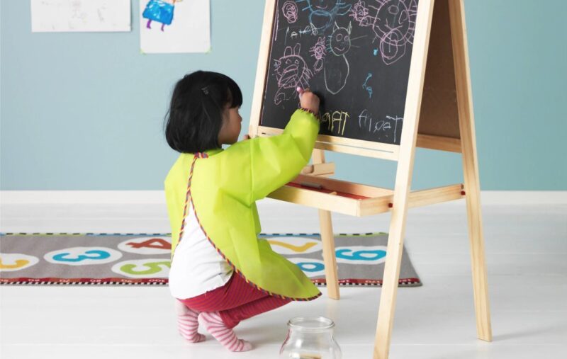 A little girl in an apron colors on an easel.