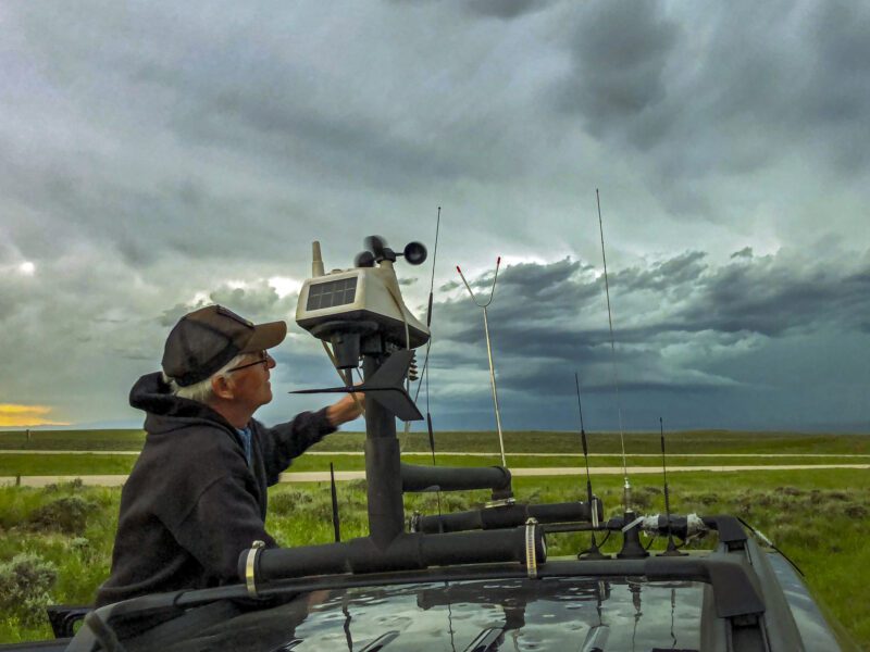 Storm-chaser adjusts the rooftop weather station on his chase vehicle as a severe storm builds in the background- science careers