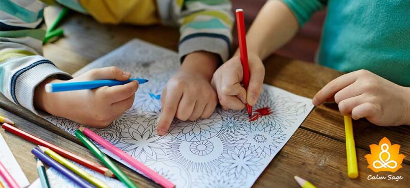 Two children sit at desks and color a mandala with colored pencils