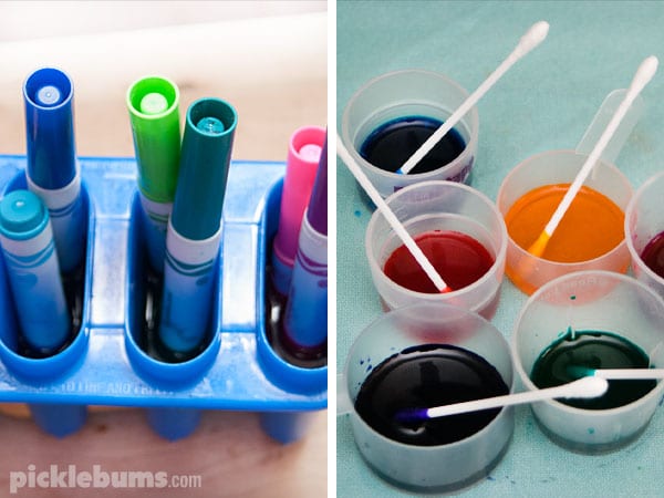 on the left, a blue bin holding 6 magic markers, on the right 6 plastic cups with colored liquid inside and a cotton swab - recycling activities
