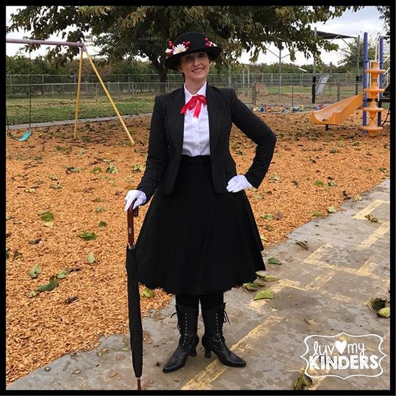 A woman is dressed as Mary Poppins in all black with a tall black hat, white button up shirt, and umbrella.- book character costume
