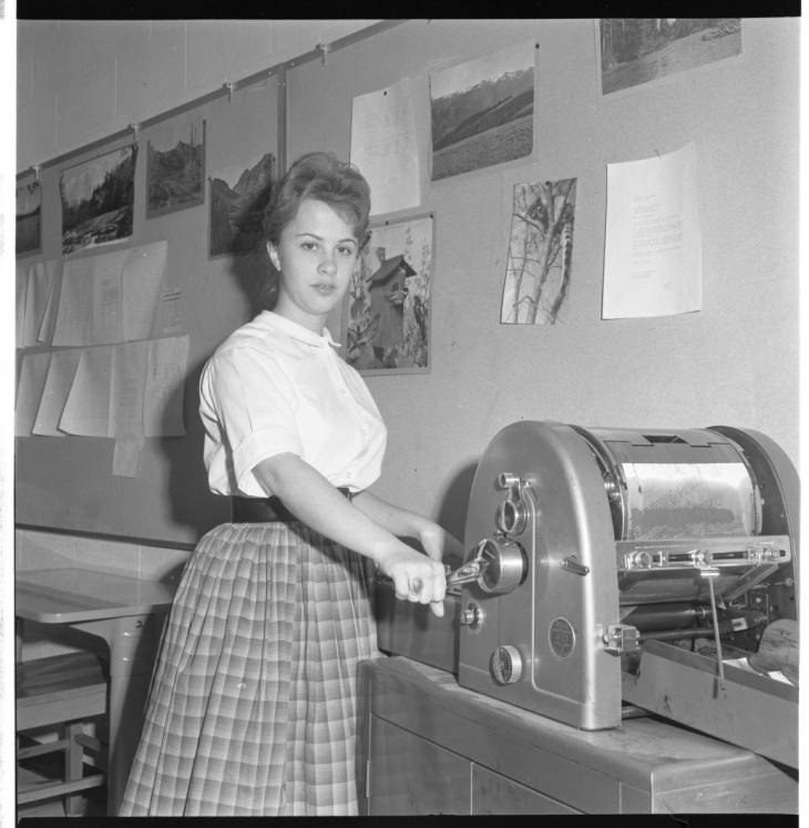 Black and white photo of a 50's teacher using a mimeograph machine -- teaching a long time