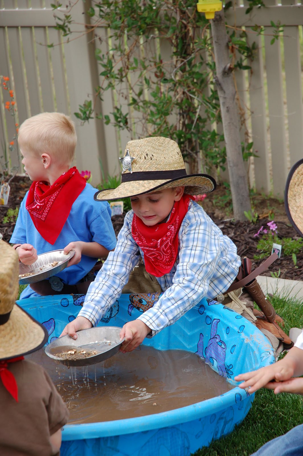 Children dressed as cowboys are sifting through mud in a kiddie pool looking for gold bits.