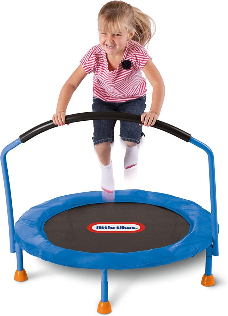 A little girl is seen jumping on a small trampoline while holding onto an attached handlebar.