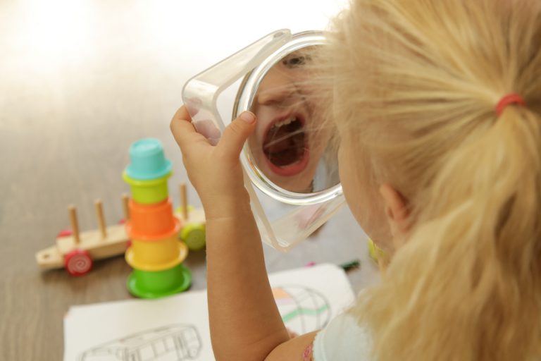 Child making sounds while looking in an hand mirror as an example of phonological awareness activities