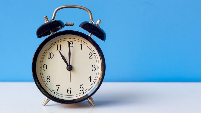 Could more half days help the teacher shortage and burnout? Alarm clock pointing to 11:00 on a white desk.