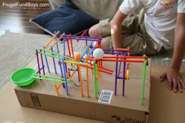 Children playing with a toy roller coaster built from drinking straws and a ping pong ball