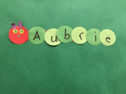 A caterpillar is constructed of construction paper. Each section of the body is a different letter that spells Aubrie.