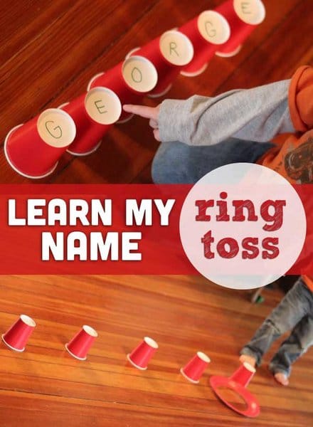 Several red solo cups are laid out with initials on them spelling a name. A child's finger is pointing to them. A red paper plate has a hole cut in it.