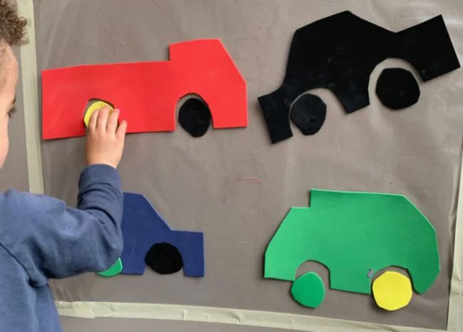 Toddler putting together car pieces on a wall covered in contact paper