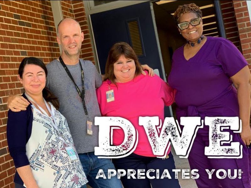 Four members of a school custodial staff gathered in front of the school, with a note saying DWE appreciates you, in honor of National Custodian Day