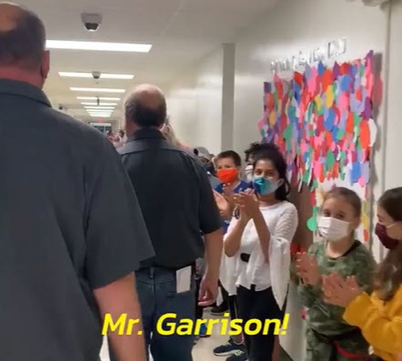 School custodians walking through a hallway filled with students thanking them for their hard work. Text reads Mr. Garrison!