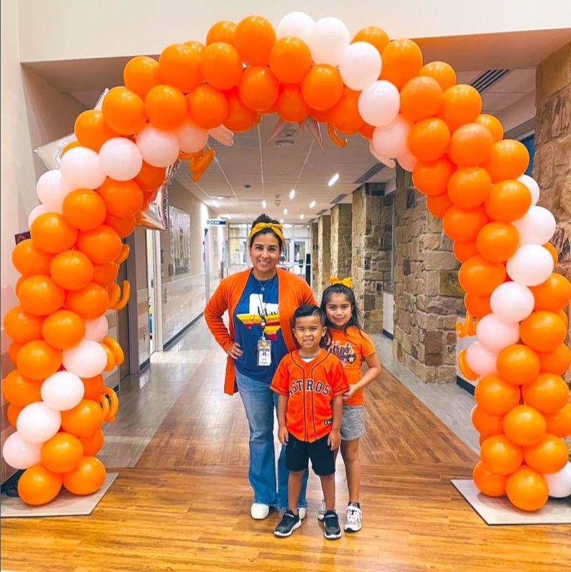 Students and teachers dressed in orange, standing beneath an orange and white balloon arch celebrating National Unity Day during Bullying Prevention Month