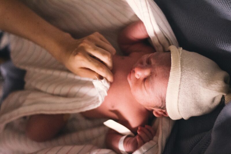 Newborn baby with hand putting blanket on.