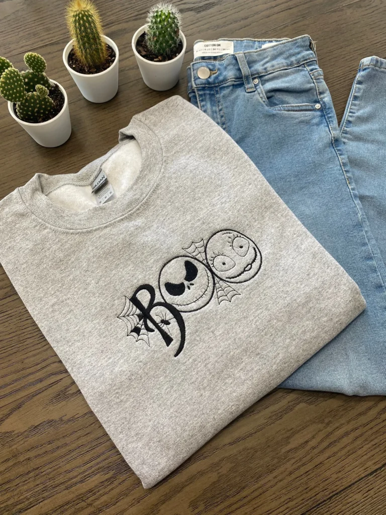 A folded gray sweatshirt has BOO embroidered on it. The O's are made to look like characters from the movie Nightmare Before Christmas.