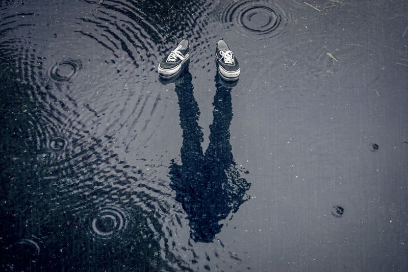 A pair of sneakers and a person's shadow in a puddle