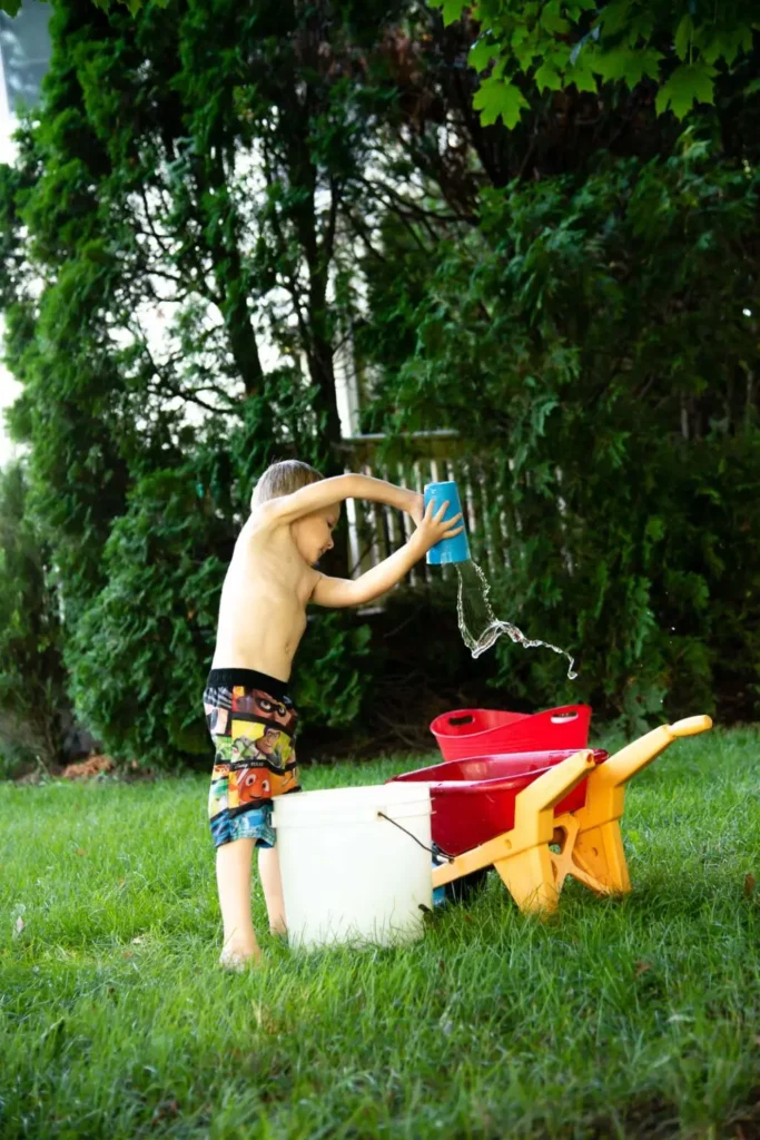 boy pouring water from a bucket into a larger bucket for a water activity
