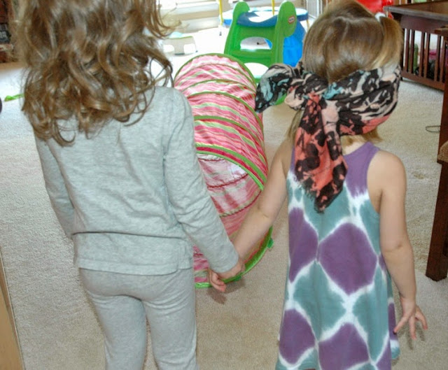 Two children stand facing an obstacle course and one is blindfolded. They are holding hands.
