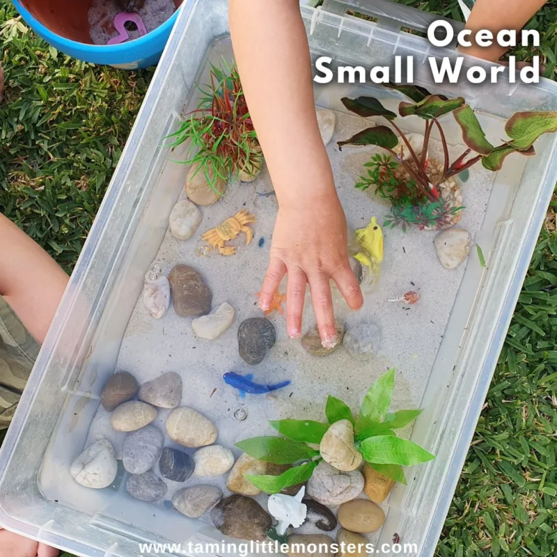 hands on a bin with water and rocks and ocean toys