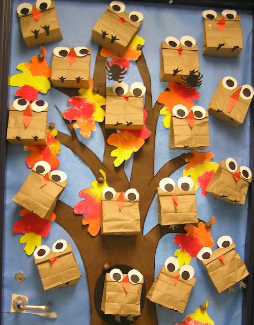 A classroom door is covered in blue paper with a brown construction paper tree. Fifteen or so owls are on the tree and are made of brown paper bags with big google eyes. Fall foliage is also shown.