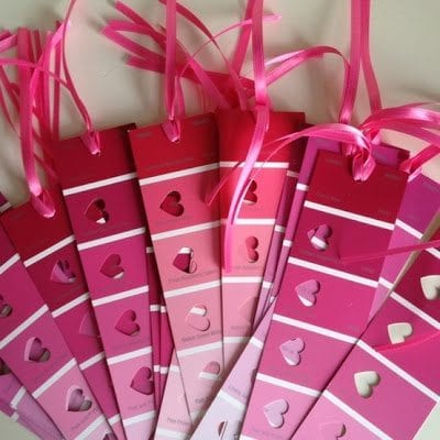 Pile of paint strips in shades of red and pink made into bookmarks with heart-shaped cut outs and pink ribbon on top