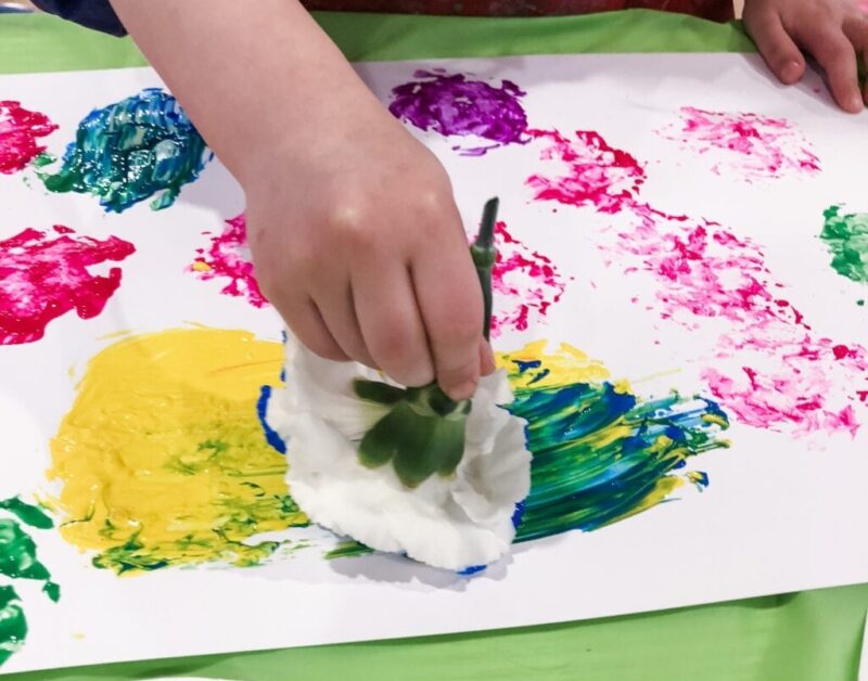 A child uses a white carnation as a paintbrush to create a colorful painting