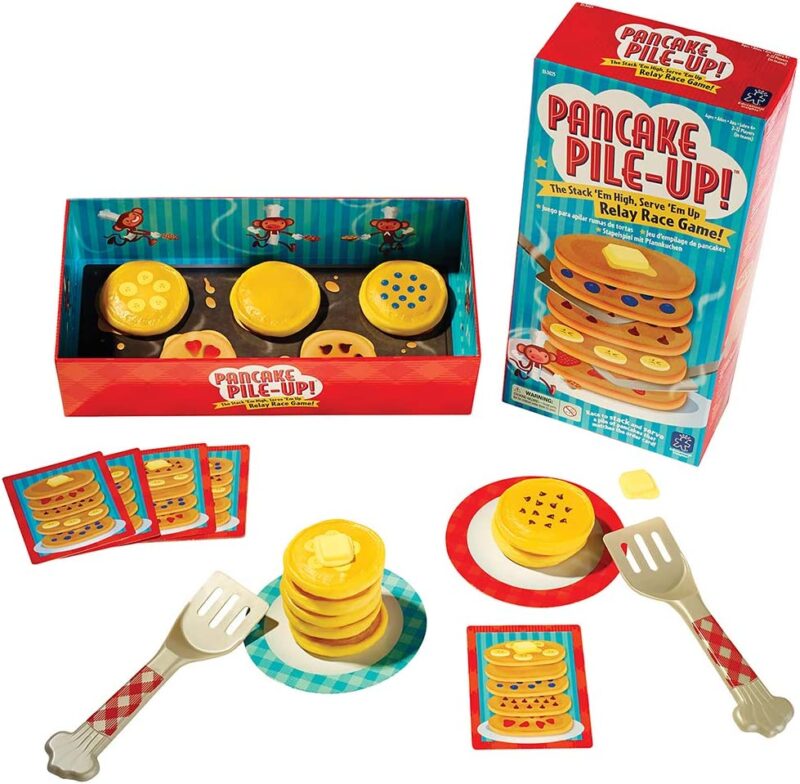 A game box shows pancakes piled up. There are plastic pancakes also shown on plates with toy forks. Game cards are pictured. (best board games for preschoolers)