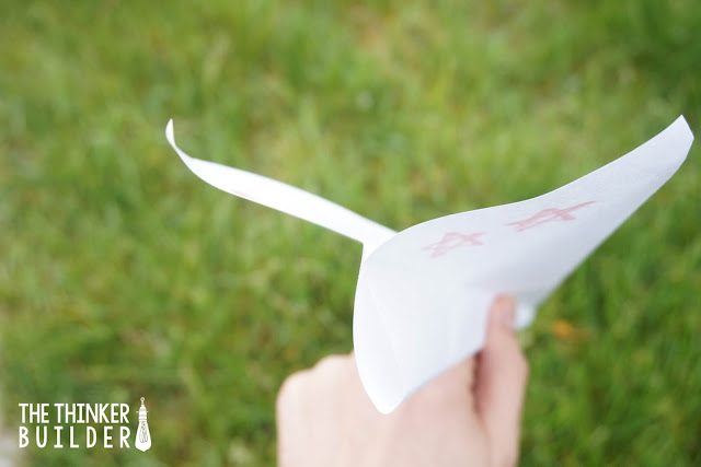 child's hand holding a paper airplane with green grass in the background