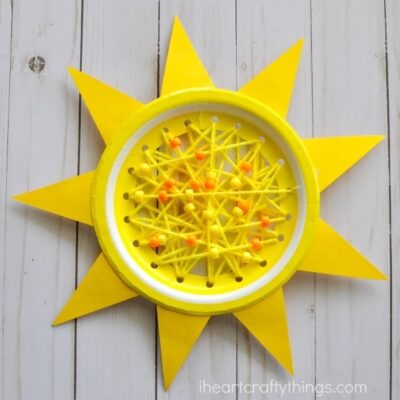 Yellow paper plate with colored paper shaped like rays of the sun around the border and yarn and beads strung across the middle, as an example of summer crafts for kids