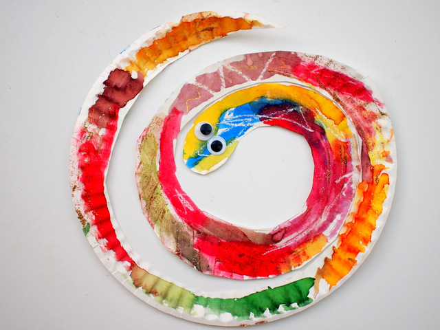 A paper plate is cut into a spiral and painted with watercolor paints. Googly eyes havebeen glued on.