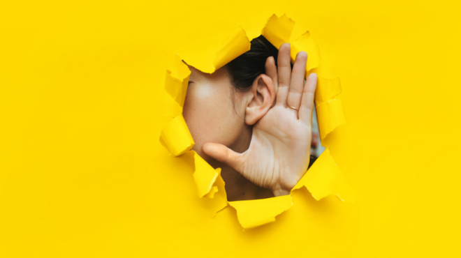 Close-up of a woman's ear and hand through a torn hole in the paper. Yellow background, copy space
