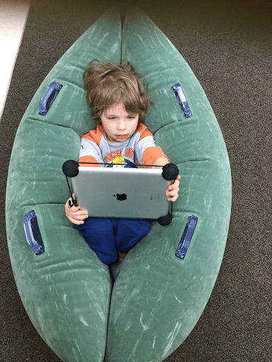 Child sitting in pea-shaped bean bag holding a tablet