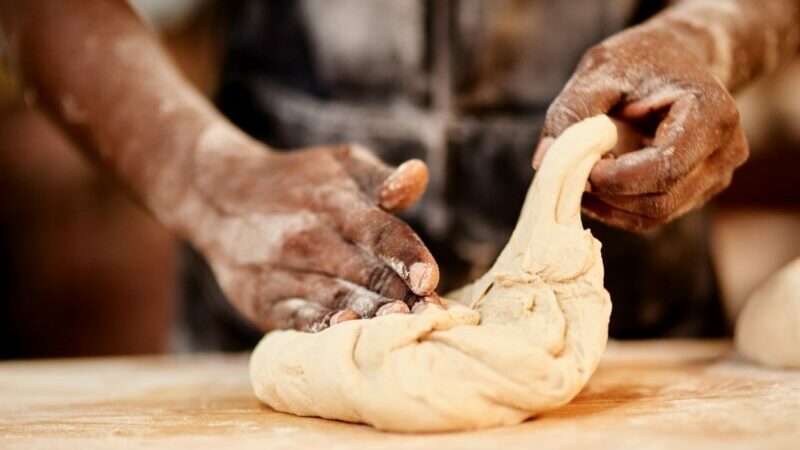 Black hands kneading dough on a board