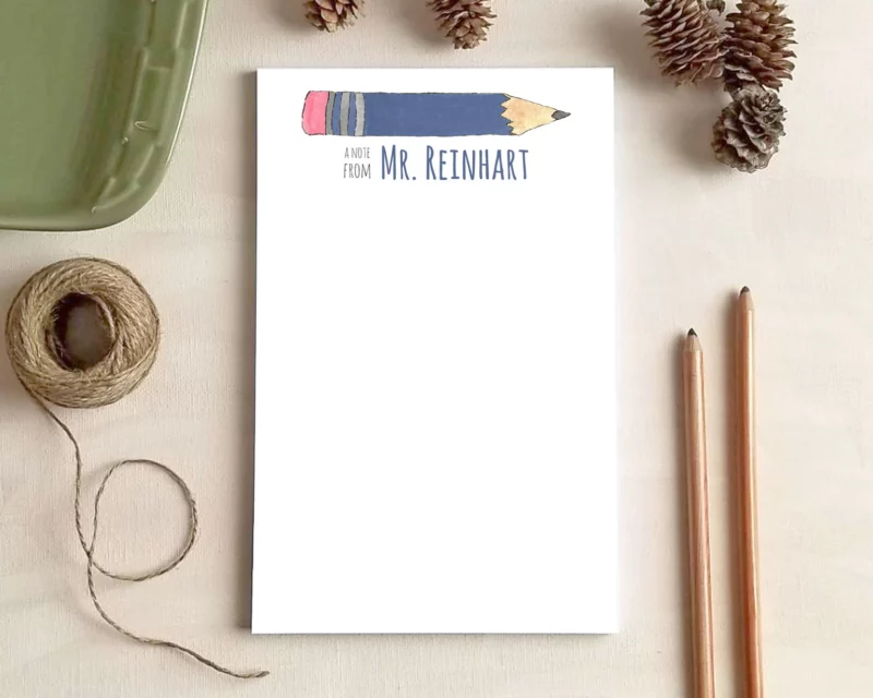 Personalized teacher notepad with a blue pencil illustration for Mr. Reinhart on a desk with fall decor.