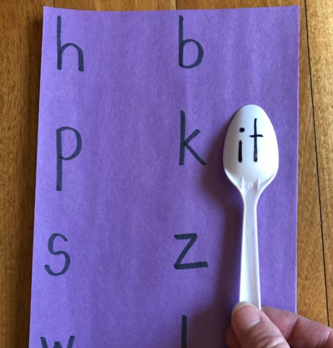 Child holding a spoon with ending letters written on the back next to beginning letters to spell words