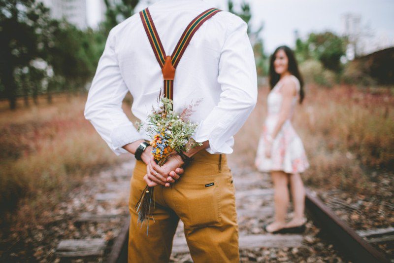 Figure holding flowers behind its back, with a woman turning to look in the background