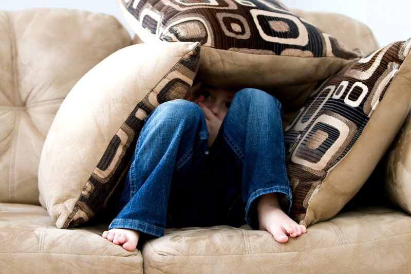 Child hiding behind a heap of pillows on a beige couch (Picture Writing Prompts)