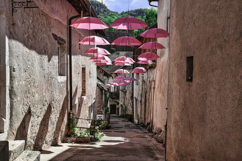 A sunny alleyway with pink umbrellas strung across it