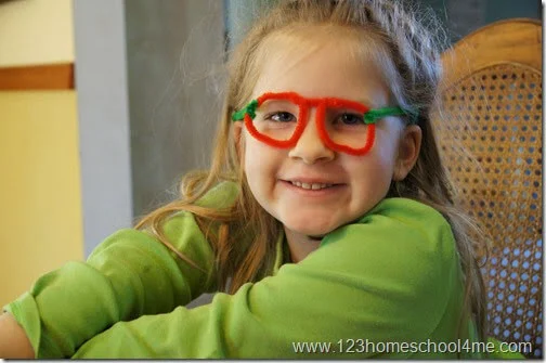 A little girl is wearing a pair of glasses made from red and green pipe cleaners.