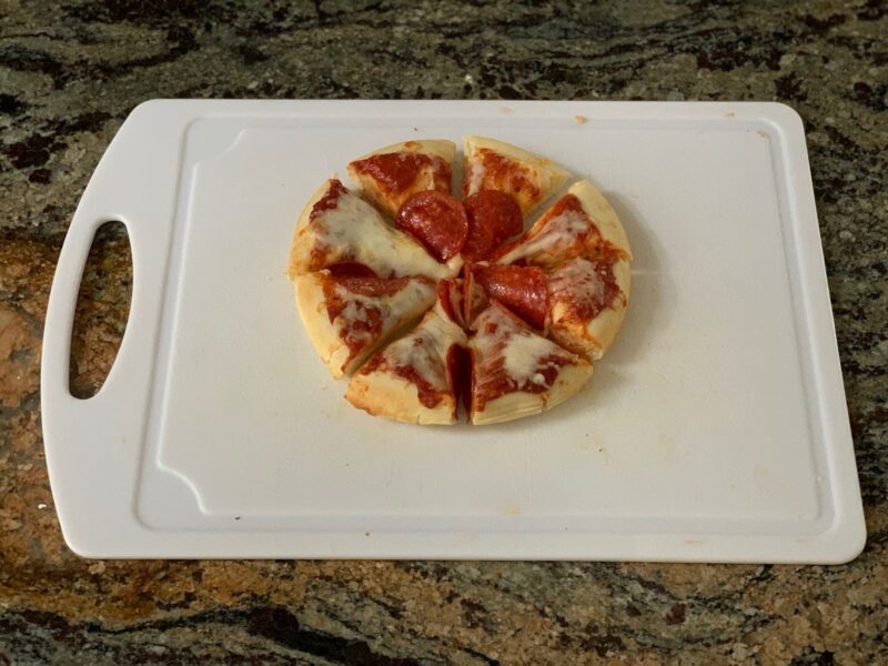 A pepperoni pizza cut into wedges sits on a white cutting board