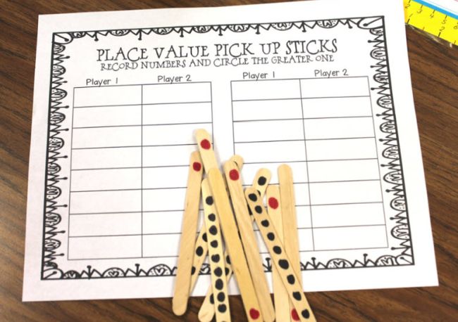 Wood craft sticks, some with 10 dots and some with one dot, and a printable worksheet labeled Place Value Pick Up Sticks, used for first grade math games