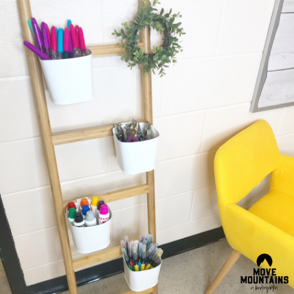 A ladder like plant stand is shown with white cups attached that are filled with art supplies.